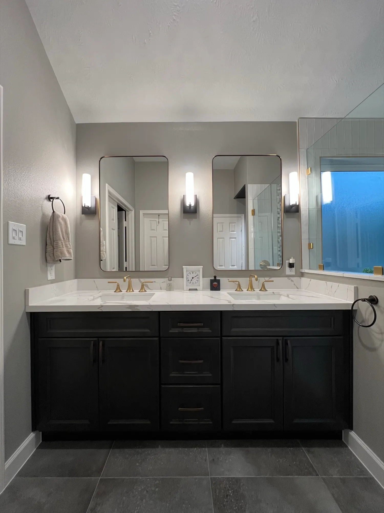 Primary bath with a black shaker double vanity, marble-look top, brass faucets and slate-look tile floor