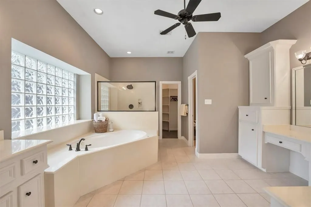 Before: primary bath with a builder-grade corner tub under a glass block window